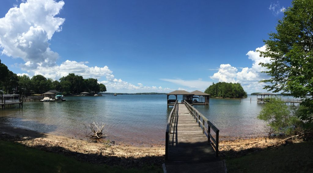 A panoramic picture of a lake with a dock in summer